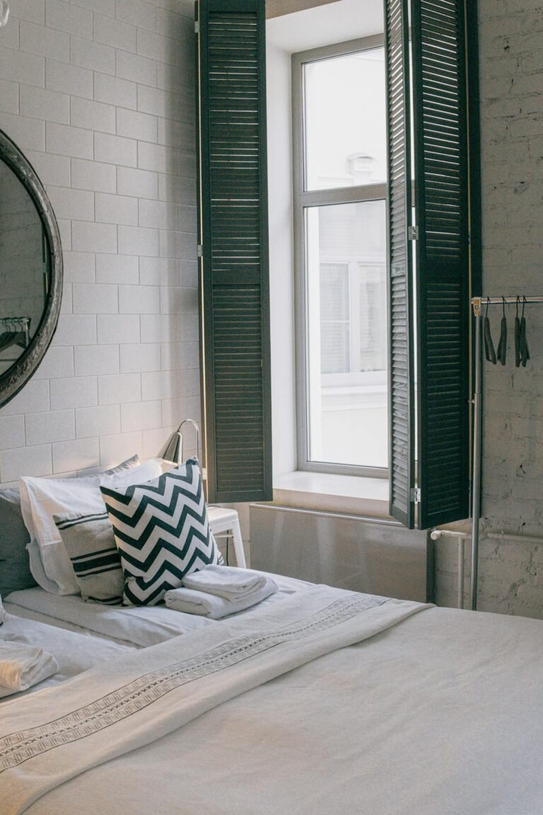 A cozy and stylish bedroom featuring modern decor and a sunlit window with shutter panels.