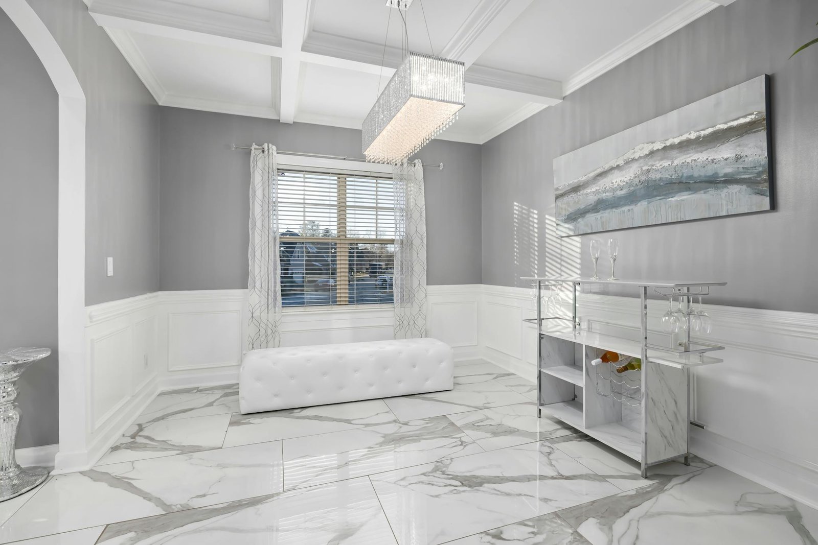Bright minimalist room with luxury marble flooring and modern decor, featuring chandelier and abstract art.